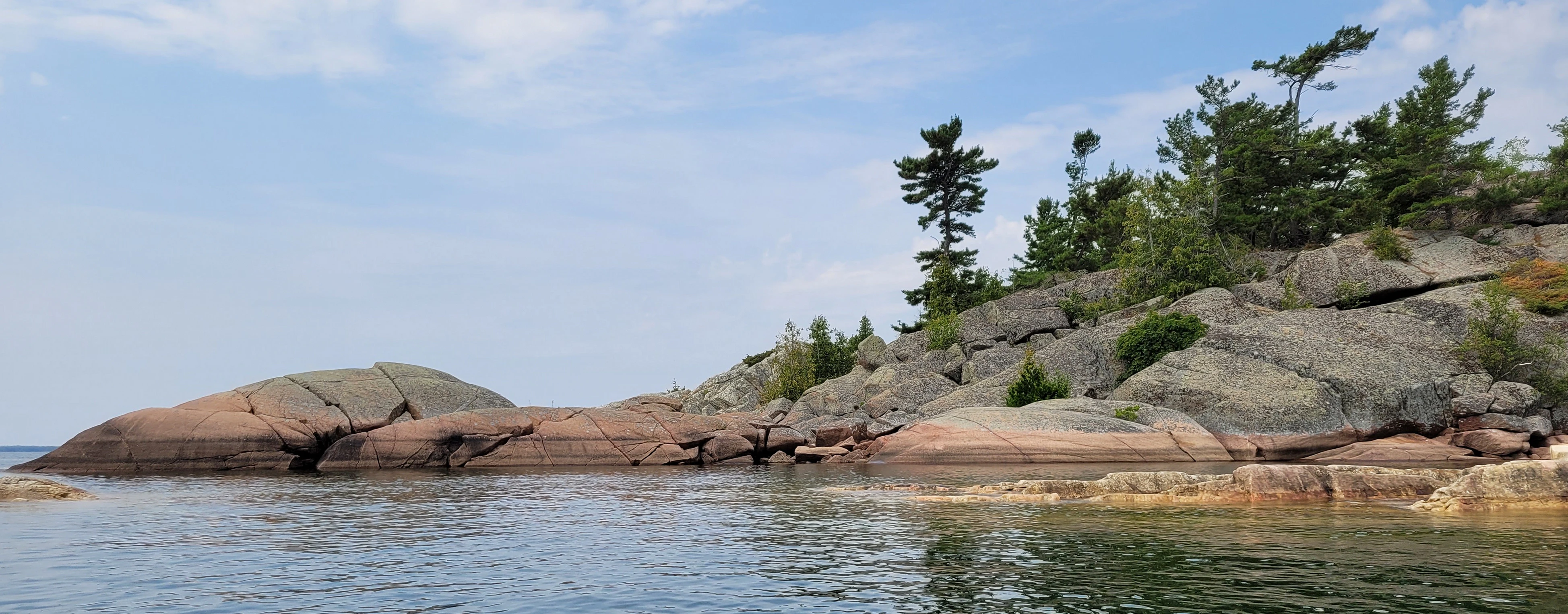 Western Shoreline of the Benjamind islands with red granite rock, white quartzite,
                trees and clear water